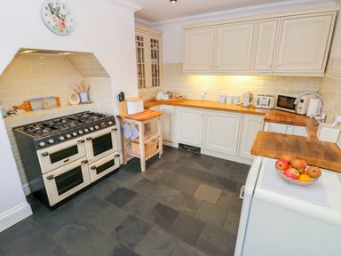 A kitchen with a stove, wooden countertops, cabinets, a sink, and a bowl of fruit at Castle School House in Kidwelly