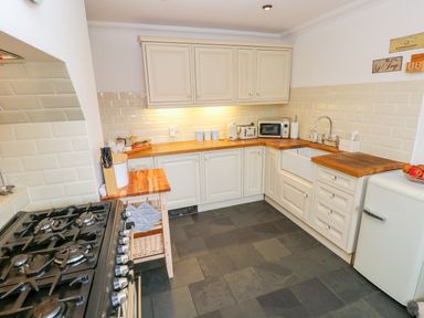 A kitchen with cream cabinets wooden countertops a gas stove a white sink a microwave and a small refrigerator at Castle School House in Kidwelly