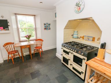 A kitchen with a stove a small wooden table with two chairs and a window at Castle School House in Kidwelly