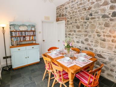 A dining room with a wooden table set for six and a light blue cabinet holding books at Castle School House in Kidwelly