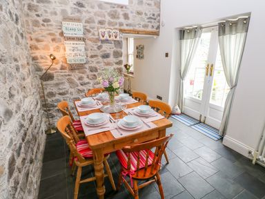 A dining area with a wooden table set for six people and a stone wall at Castle School House in Kidwelly