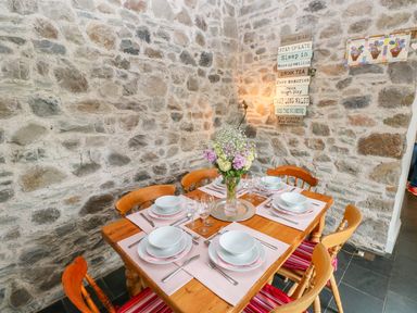 A dining table set for six with plates glasses and flowers against a stone wall at Castle School House in Kidwelly