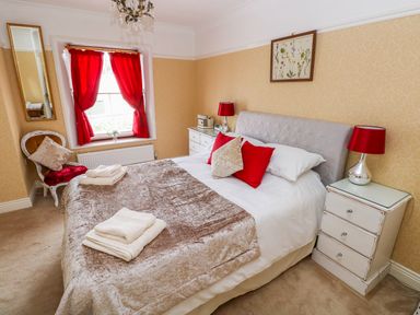 A bedroom with a bed towels red curtains and bedside tables at Castle School House in Kidwelly