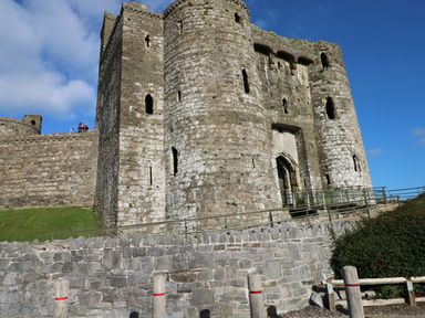 A stone castle with multiple towers and small windows behind a stone wall and green grassy area at Castle School House in Kidwelly