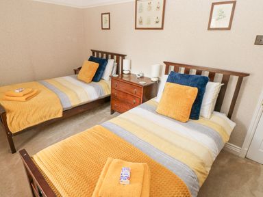 A bedroom with two single beds a wooden nightstand between the beds and framed pictures on the wall at Castle School House in Kidwelly