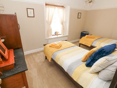 A bedroom with two single beds, bedding with yellow and gray stripes, towels on beds, a window with curtains, and a wooden dresser at Castle School House in Kidwelly