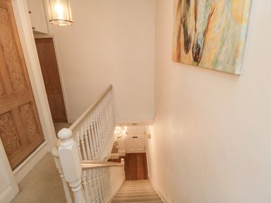 A staircase with white railing leading down to a hallway with wooden doors and a chandelier light at Harriet's Cottage in Briggswath