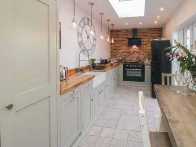 A kitchen with gray cabinets wooden countertops a brick wall with stove a dining table with flowers and chairs at Harriets Cottage in Briggswath