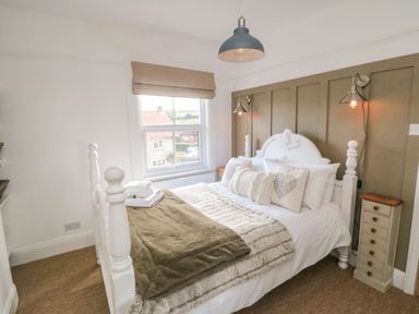 A bedroom with a white bed and brown blankets and pillows and a window with a beige blind at Harriet's Cottage in Briggswath