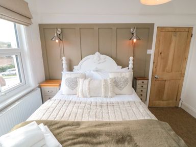A bedroom with a white bed and pillows two bedside tables with lamps and a wooden door at Harriets Cottage in Briggswath