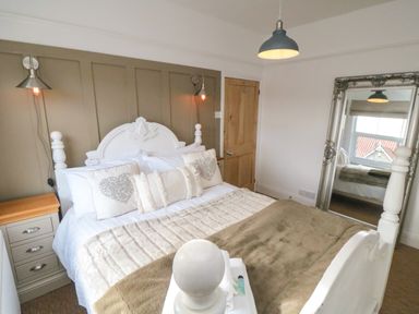 A bedroom with a white bed and pillows beside a wooden door and a large mirror at Harriets Cottage in Briggswath