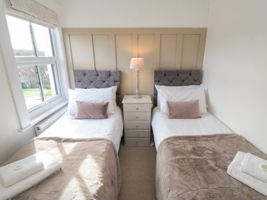 A bedroom with two single beds a bedside table with a lamp and a window at Harriets Cottage in Briggswath
