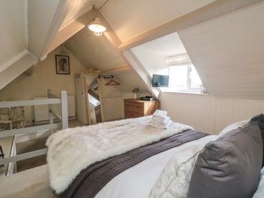 A bedroom with a bed folded towels a chest of drawers a wall mirror and a small television at Harriets Cottage in Briggswath