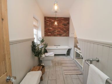 A bathroom with a bathtub toilet sink wooden bench and a plant at Harriets Cottage in Briggswath