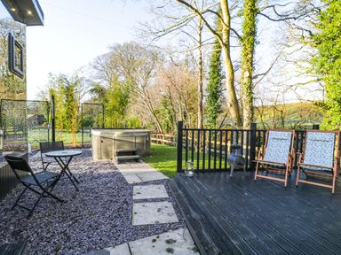 An outdoor patio area with two wooden deck chairs a small table with two metal chairs a hot tub and trees at Reflection in Longtown
