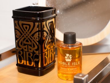 A black decorative container and a small bottle of bath and shower gel on a wooden surface at Reflection in Longtown