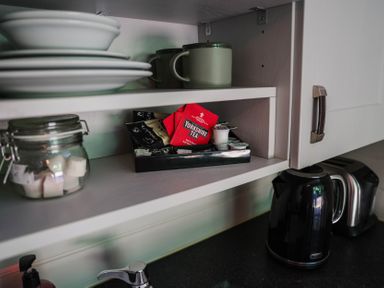 A kitchen shelf with plates, mugs, a jar of sugar, Yorkshire Tea and a kettle at Reflection in Longtown