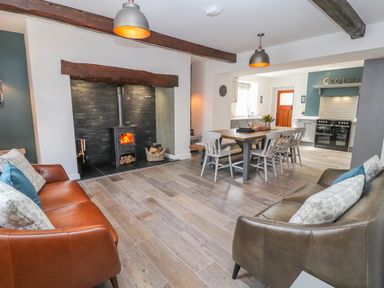 A living room with two sofas and a wood burning stove next to a dining table with chairs at Llys Alaw in Llangernyw