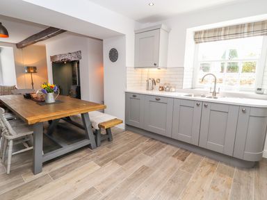 A kitchen with gray cabinets wooden dining table and window with striped blind at Llys Alaw in Llangernyw