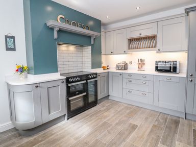 A kitchen with gray cabinets a black oven a toaster microwave and knives at Llys Alaw in Llangernyw