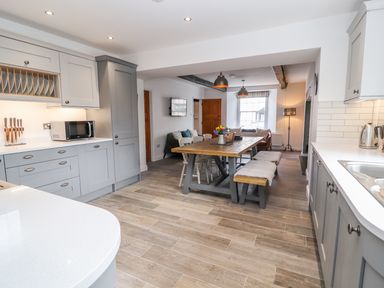 A kitchen with grey cabinets a wooden dining table chairs and benches a microwave and a kettle at Llys Alaw in Llangernyw