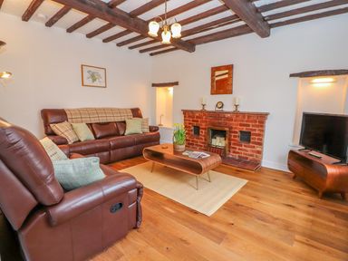 A living room with brown leather sofas a wooden coffee table a brick fireplace a television and wooden ceiling beams at Llys Alaw in Llangernyw