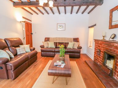 A living room with brown leather sofas a wooden coffee table with flowers a brick fireplace and exposed wooden beams at Llys Alaw in Llangernyw