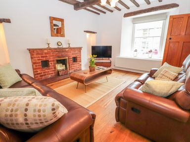 A living room with two brown leather sofas a wooden coffee table and a brick fireplace at Llys Alaw in Llangernyw