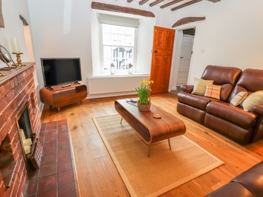A living room with a leather sofa a wooden coffee table with flowers a television on a stand and a brick fireplace at Llys Alaw in Llangernyw