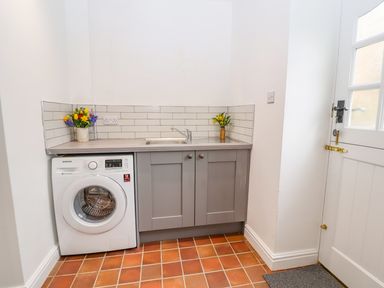 A laundry room with a washing machine under a countertop with a sink and flowers on the counter at Llys Alaw in Llangernyw