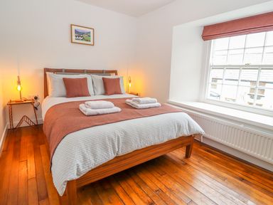 A bedroom with a double bed two bedside tables with lamps a large window and wooden floor at Llys Alaw in Llangernyw