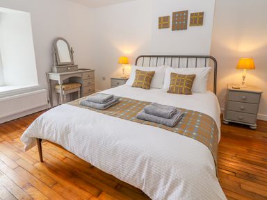 A bedroom with a double bed bedside tables with lamps a dressing table and a window at Llys Alaw in Llangernyw