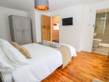 A bedroom with a bed a towel on the bed a wooden floor a wardrobe a door a wall mounted tv and an ensuite bathroom at Llys Alaw in Llangernyw