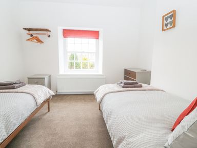 A bedroom with two single beds side tables drawers window with red blind and wall-mounted clothes rack at Llys Alaw in Llangernyw