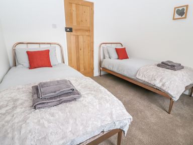 A bedroom with two single beds with white bedding, red pillows, folded towels, a wooden door, and a framed artwork on the wall at Llys Alaw in Llangernyw