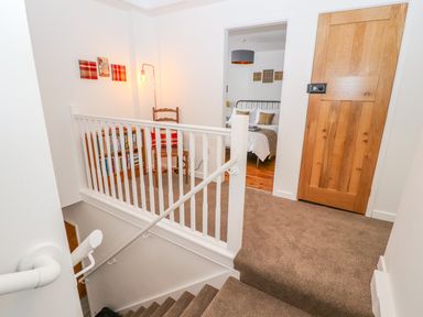 A carpeted staircase landing with a wooden door an open doorway leading to a bedroom a wooden chair a small bookshelf and wall decorations at Llys Alaw in Llangernyw