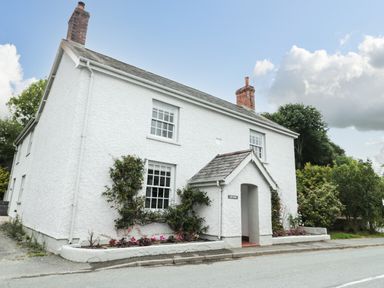 A white two-story house with two chimneys and climbing plants by the windows at Llys Alaw in Llangernyw
