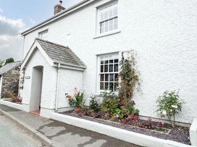 The exterior of a white textured house with two windows a small entrance porch and a flower bed along the wall at Llys Alaw in Llangernyw