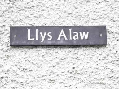 A black rectangular sign with white text reading Llys Alaw mounted on a white textured wall at Llys Alaw in Llangernyw