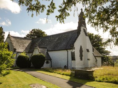An exterior view of a stone church with a slate roof surrounded by grass and trees at Llys Alaw in Llangernyw