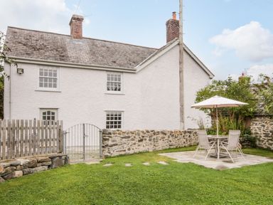 A yard with a green lawn table chairs and umbrella outside a white two story house with stone walls at Llys Alaw in Llangernyw