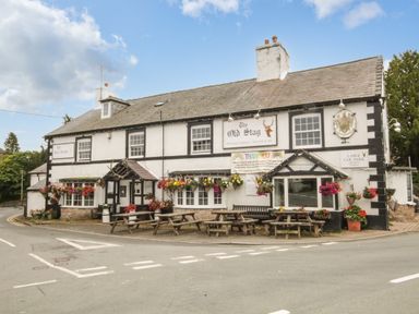 An exterior view of a pub with hanging flower baskets and picnic tables on the sidewalk at The Old Barn in Manchester