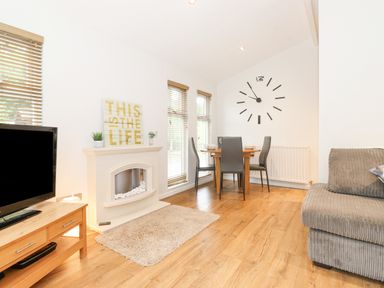 A dining area with table and chairs next to a wall clock and a living room with a TV wooden stand and fireplace at 10 Thirlmere White Cross Bay near Troutbeck Bridge