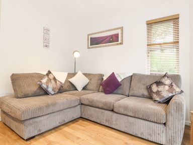 A corner sofa with cushions and a floor lamp next to a window with blinds at 10 Thirlmere White Cross Bay near Troutbeck Bridge