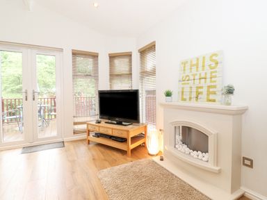 A living room with a television on a wooden stand and a fireplace with decor at 10 Thirlmere White Cross Bay near Troutbeck Bridge