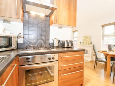 A kitchen with a stove, oven, microwave, kettle, toaster, and dining table with chairs at 10 Thirlmere White Cross Bay near Troutbeck Bridge