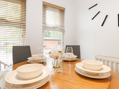 A dining table set with white bowls, plates, wine glasses, and a vase with white flowers at 10 Thirlmere White Cross Bay near Troutbeck Bridge