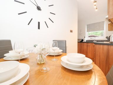 A dining table set with white dishes and wine glasses in a kitchen with wooden cabinets at 10 Thirlmere White Cross Bay near Troutbeck Bridge