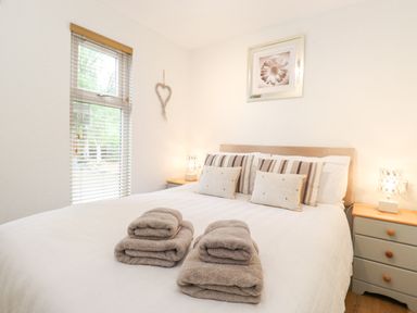 A bedroom with a bed with folded towels and cushions near a window at 10 Thirlmere White Cross Bay near Troutbeck Bridge