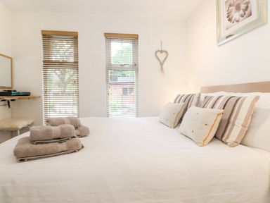 A bedroom with a bed with pillows and folded towels near windows with blinds and a wall decoration at 10 Thirlmere White Cross Bay near Troutbeck Bridge